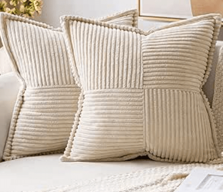 Deux coussins en velours crème avec des motifs de tissu côtelé, placés sur un canapé.